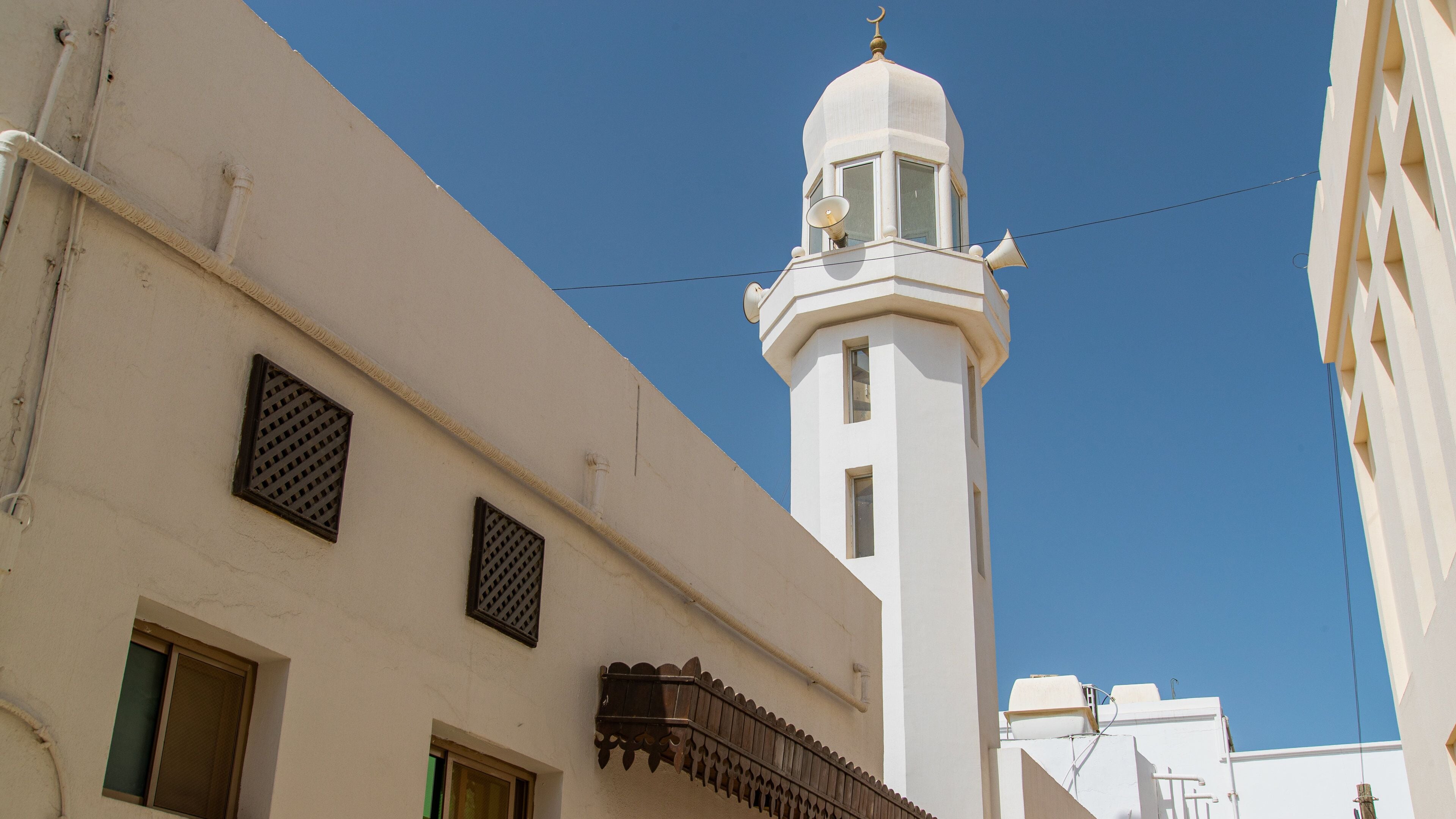 A white building with a tall minaret, a clear blue sky, and a power line.