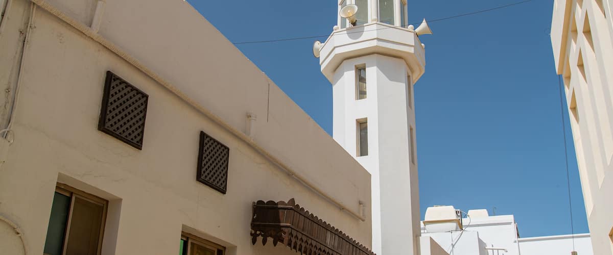 Ein weißes Gebäude mit einem hohen Minarett, blauem Himmel und einer Stromleitung.