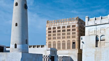 A tall white tower with arched windows and a building with a patterned facade.