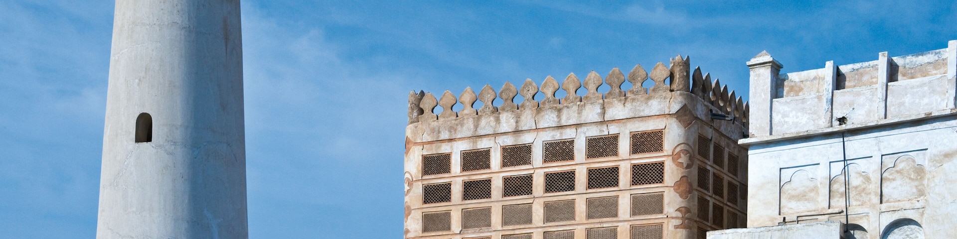 Una torre alta y blanca con ventanas arqueadas y un edificio con fachada decorada.