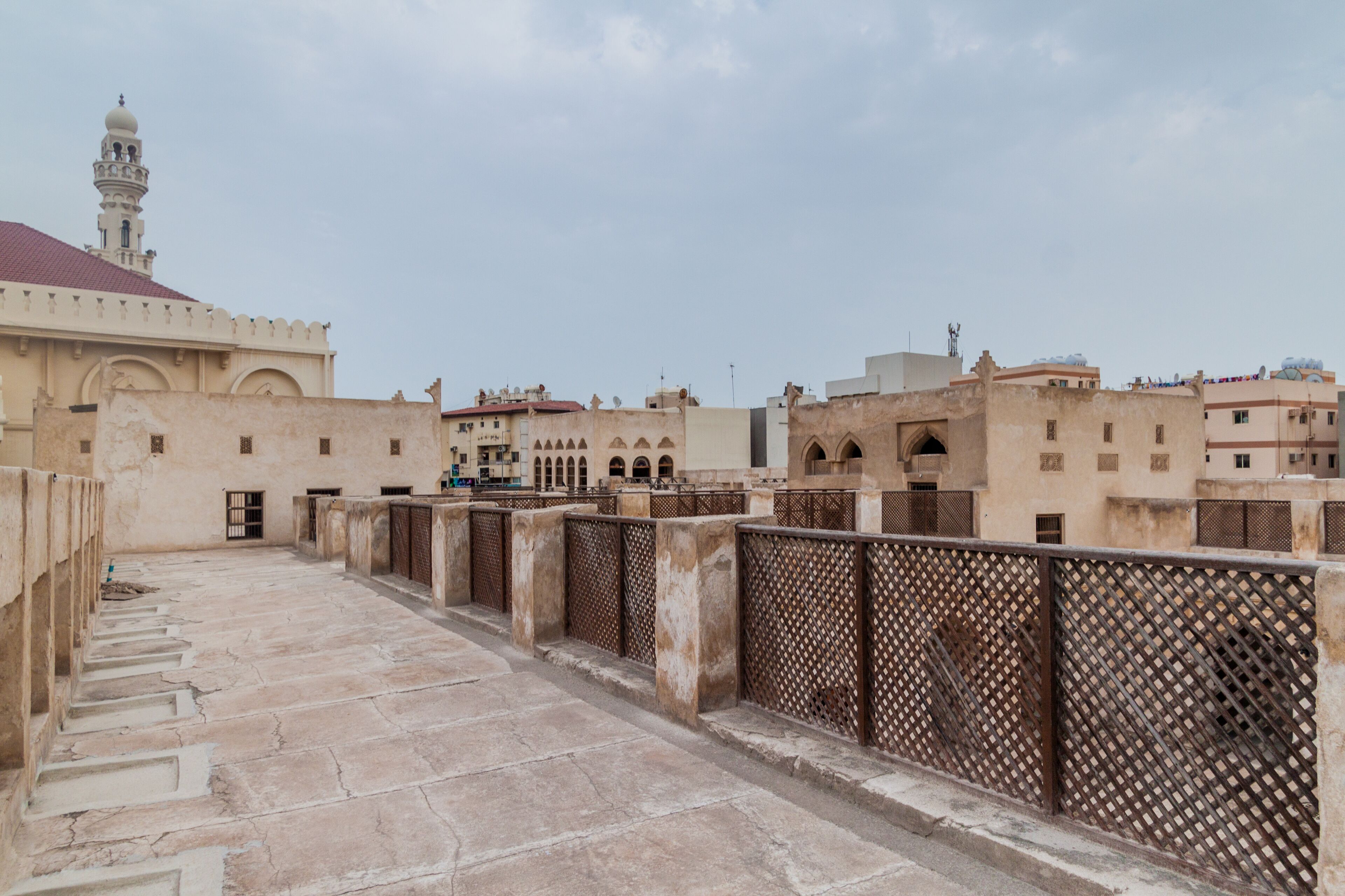 A courtyard with stone steps, a mosque with a minaret, and traditional buildings.