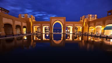 Vista nocturna de un hotel lujoso con un amplio estanque reflectante y arquitectura abovedada.