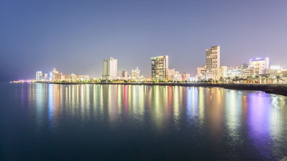 A city skyline at night with illuminated buildings reflecting on calm water.