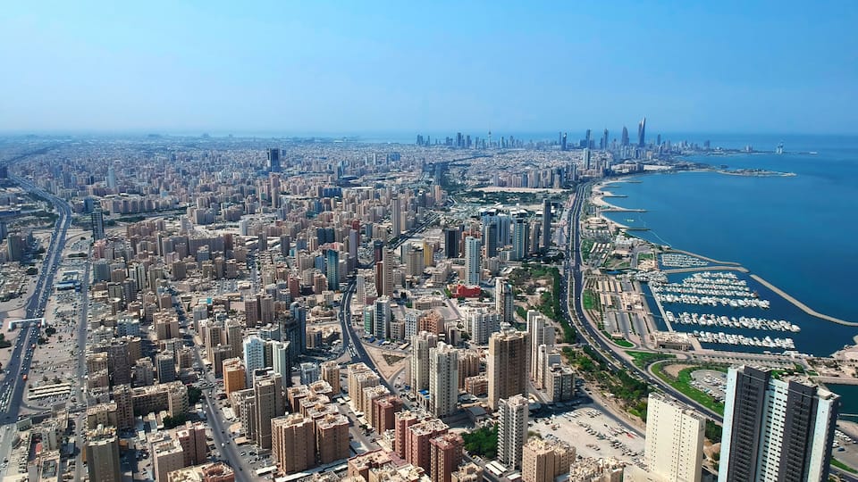 A coastal cityscape with dense urban development, a marina, and a clear blue sea.