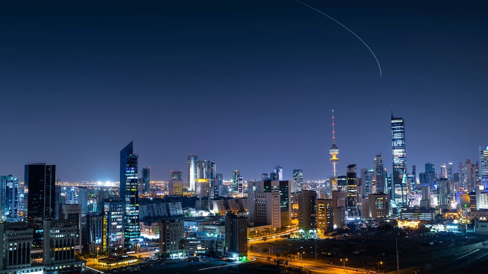 Kuwait city skyline at night with aircraft climbing from Kuwait Airport at the background