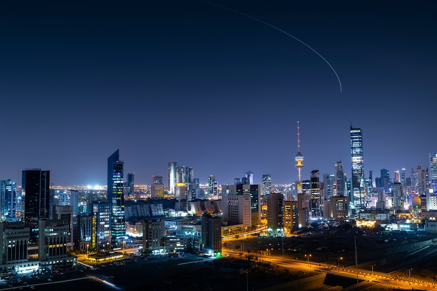 Kuwait city skyline at night with aircraft climbing from Kuwait Airport at the background