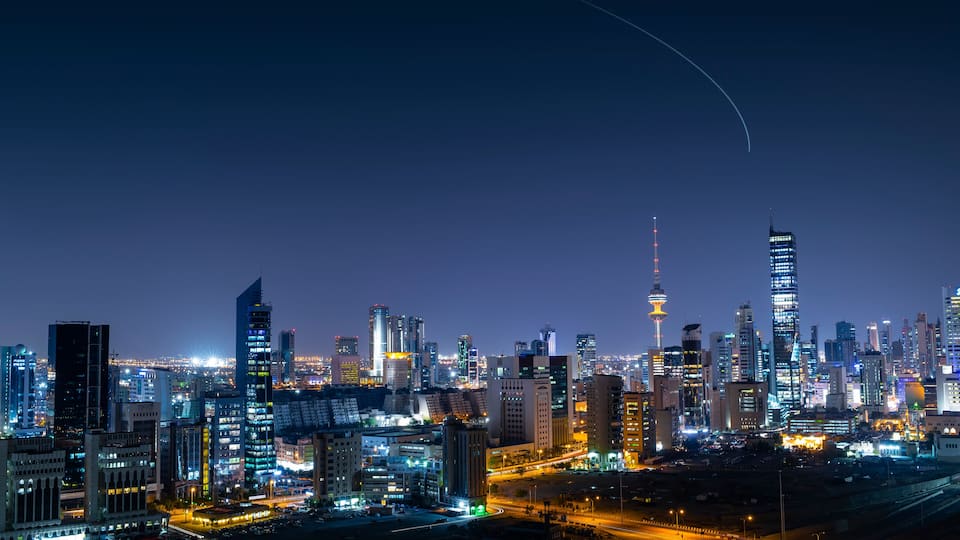 A city skyline at night with illuminated buildings and a prominent tower.