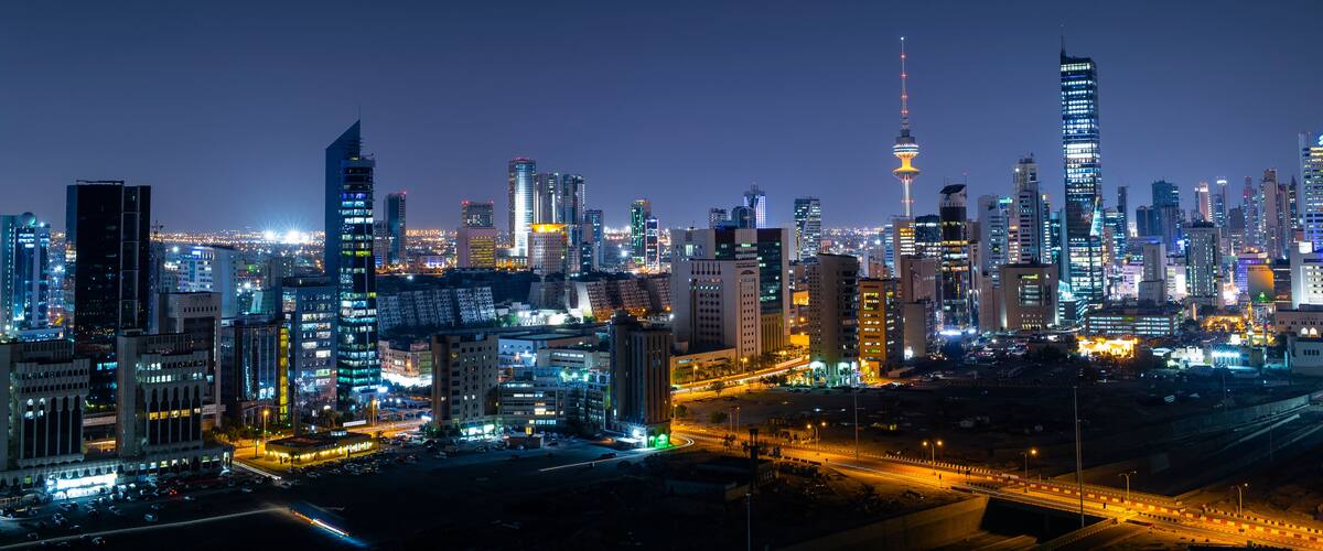 A city skyline at night with illuminated buildings and a prominent tower.