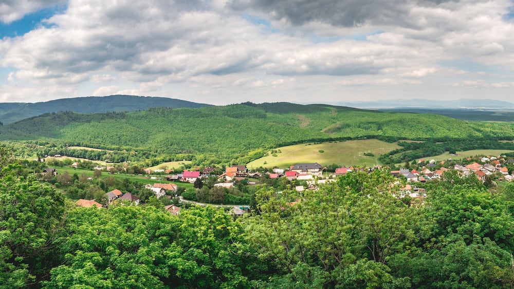 Ein üppiges, grünes Tal mit verstreuten Häusern und sanften Hügeln unter einem teils bewölkten Himmel.