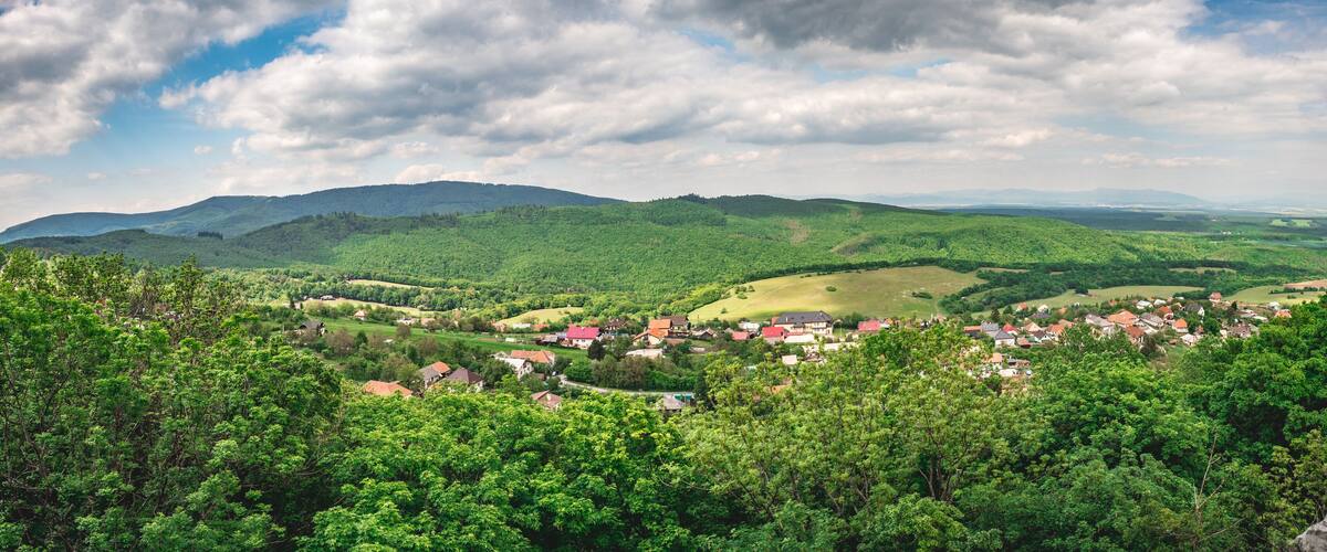 A lush green valley with scattered houses and rolling hills under a partly cloudy sky.