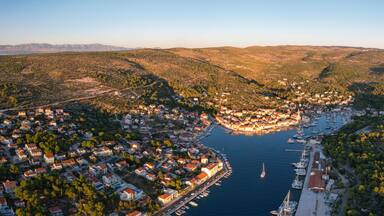 A coastal town with a marina, surrounded by hills and dense forests.