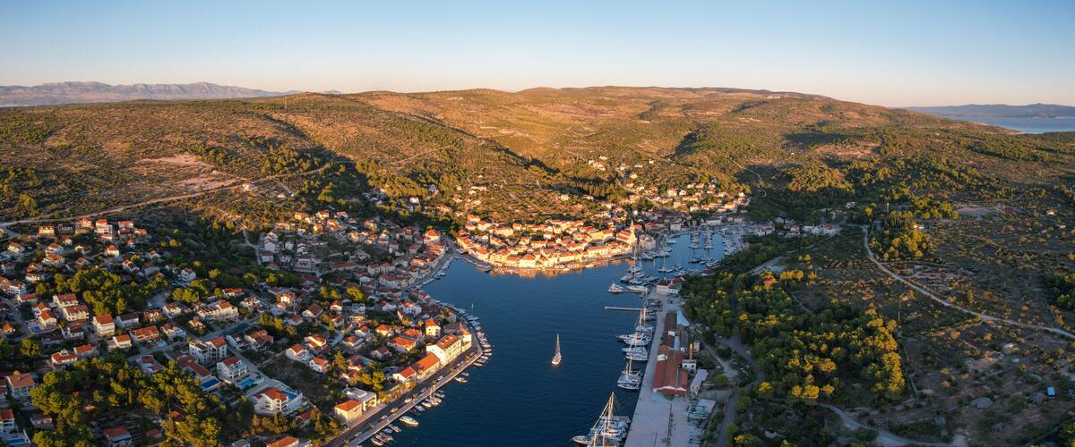 A coastal town with a marina, surrounded by hills and dense forests.