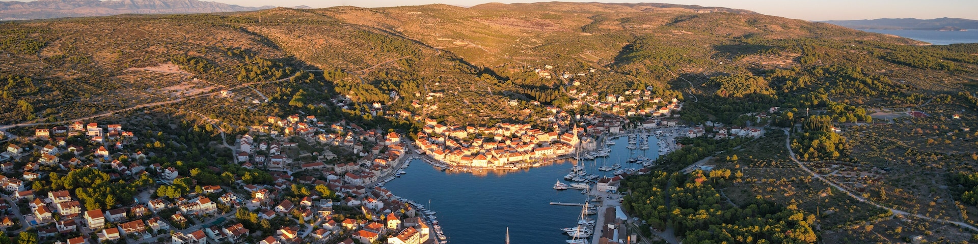 A coastal town with a marina, surrounded by hills and dense forests.