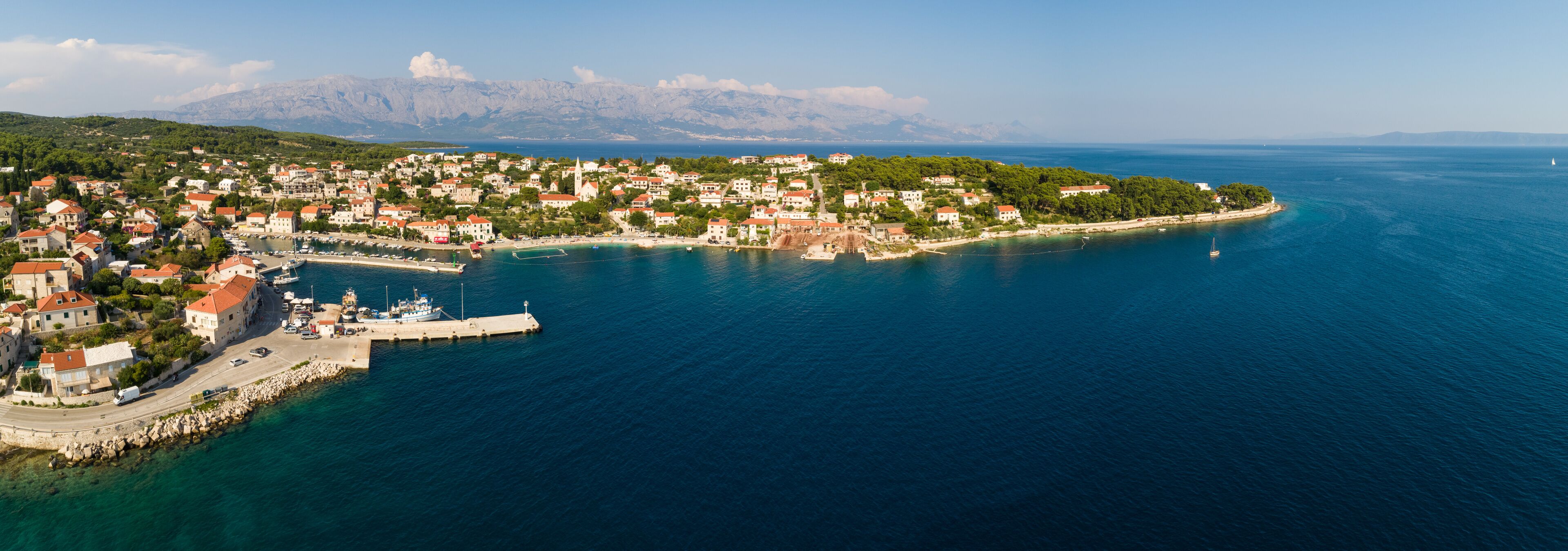 A coastal town with a marina, boats, and a mountainous backdrop.