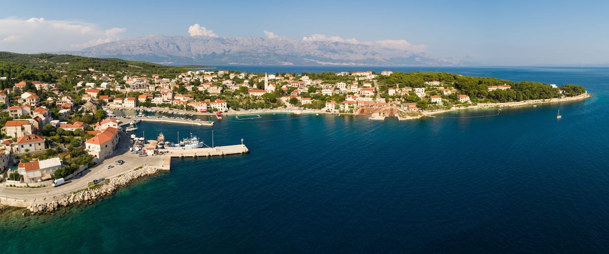 A coastal town with a marina, boats, and a mountainous backdrop.