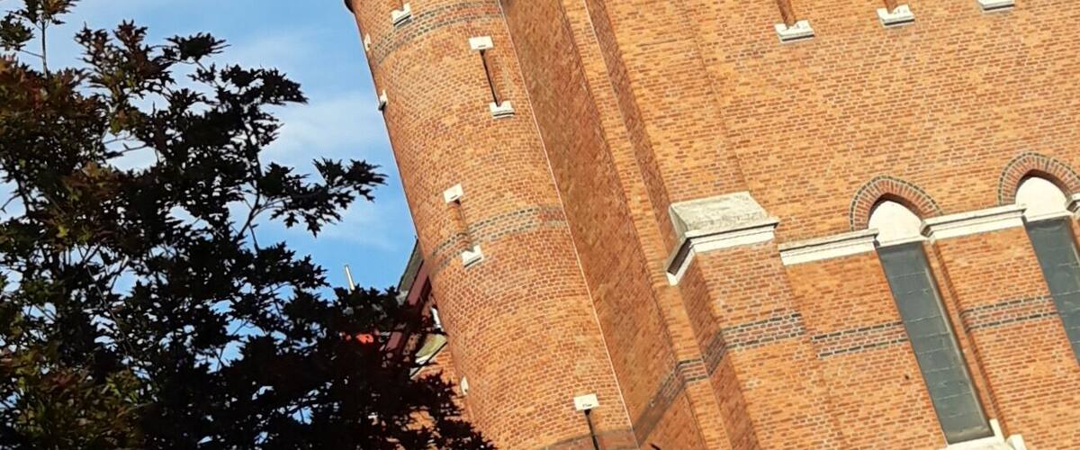 A tall brick tower with a clock and a pointed roof.