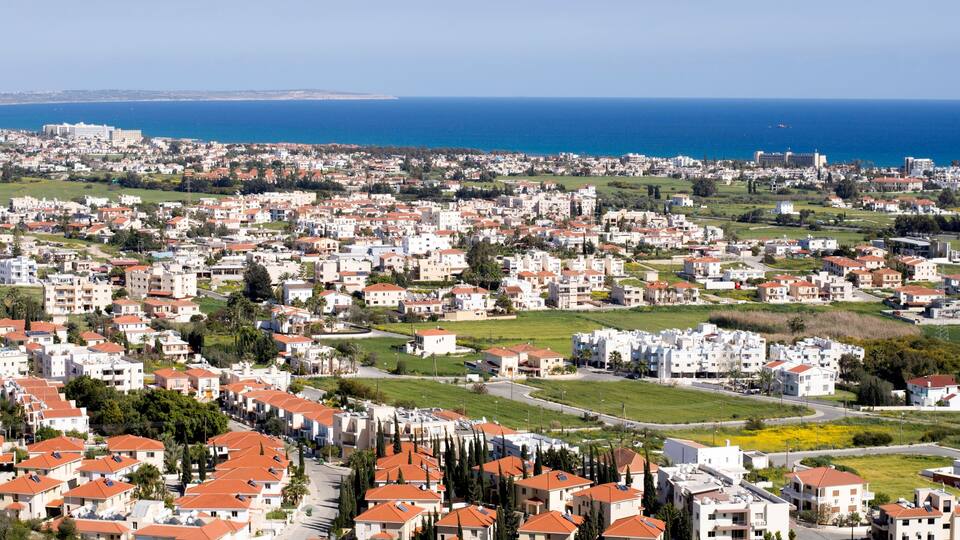 A coastal cityscape with residential buildings, green spaces, and a view of the sea.
