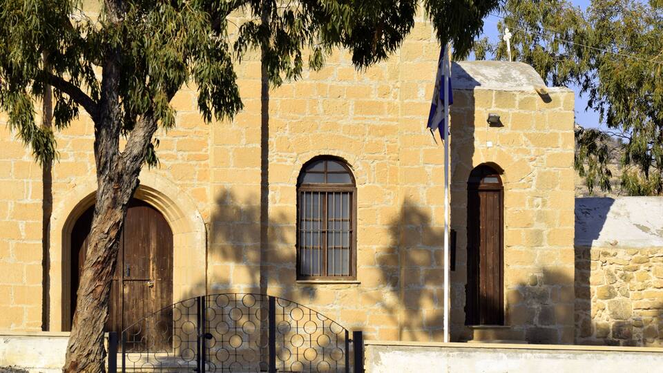A stone building with arched windows and doors, a metal gate, and a flag.