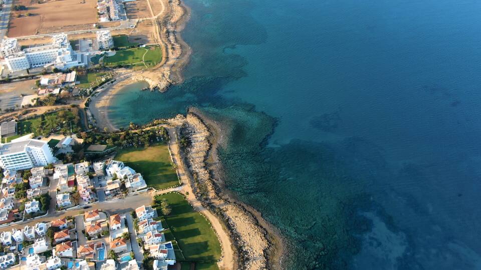 An aerial view of a coastal residential area with clear blue waters, a sandy beach, and a mix of modern and traditional architecture.
