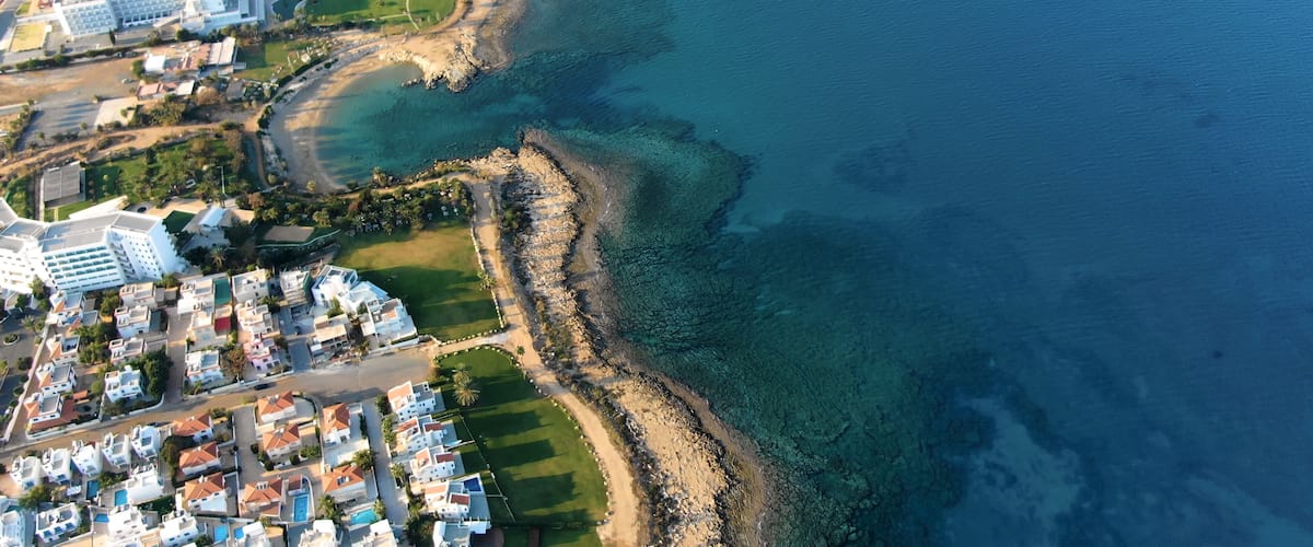 An aerial view of a coastal residential area with clear blue waters, a sandy beach, and a mix of modern and traditional architecture.