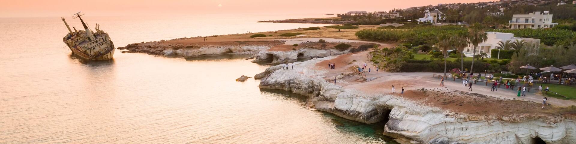 A coastal landscape with a shipwreck, rocky formations, and a promenade with people.