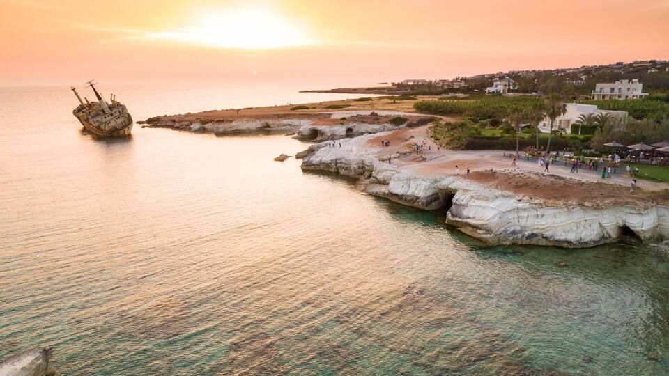 A coastal landscape with a shipwreck, rocky formations, and a promenade with people.
