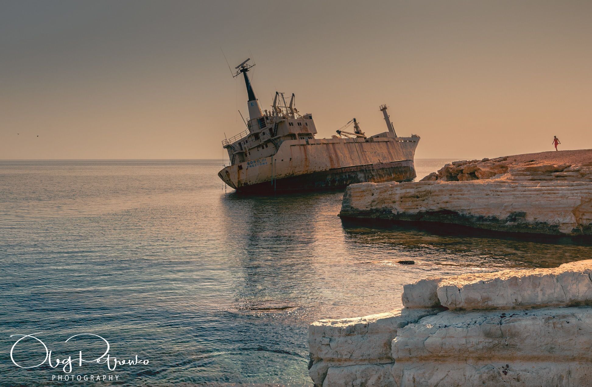 A large rusted ship stranded on a rocky shore with calm water.