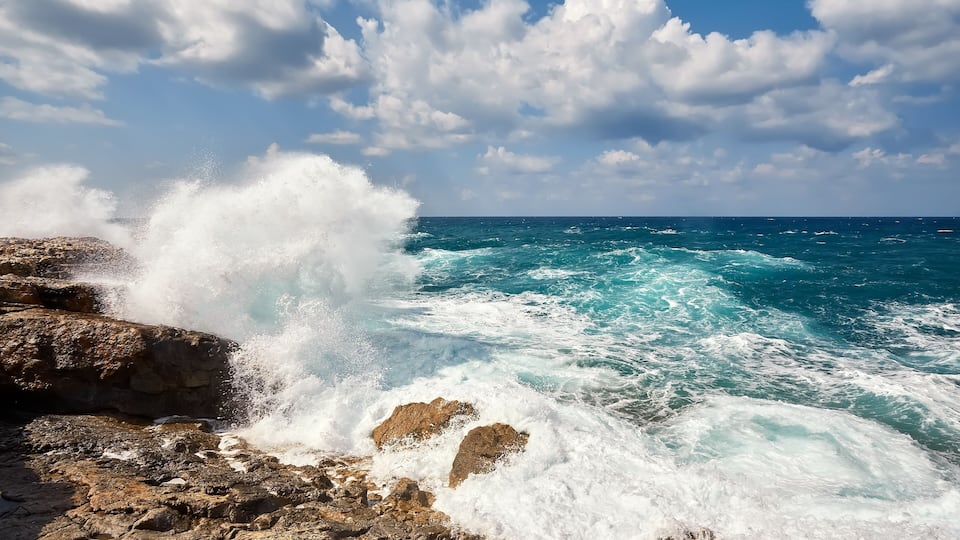 A rocky coastline with waves crashing against the rocks under a partly cloudy sky.