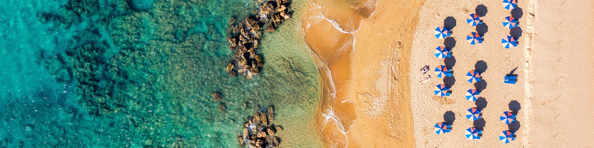 Una playa con agua turquesa cristalina, formaciones rocosas y numerosos sombrillas.