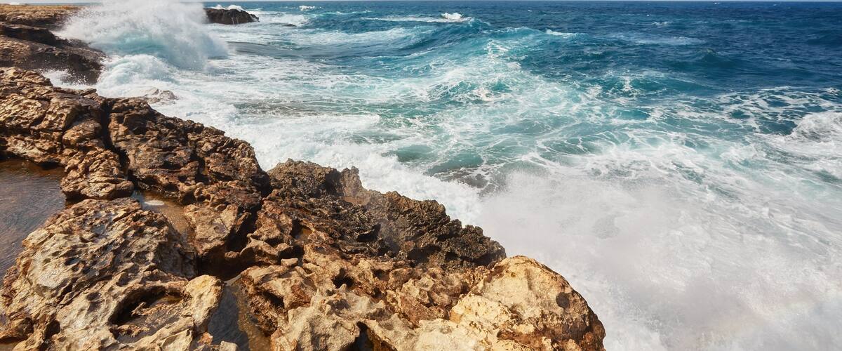 A rocky coastline with waves crashing against the rocks under a partly cloudy sky.
