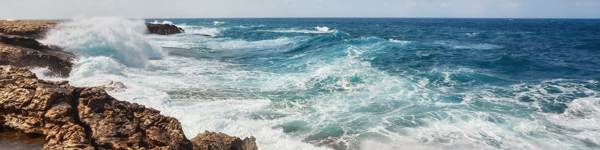 A rocky coastline with waves crashing against the rocks under a partly cloudy sky.