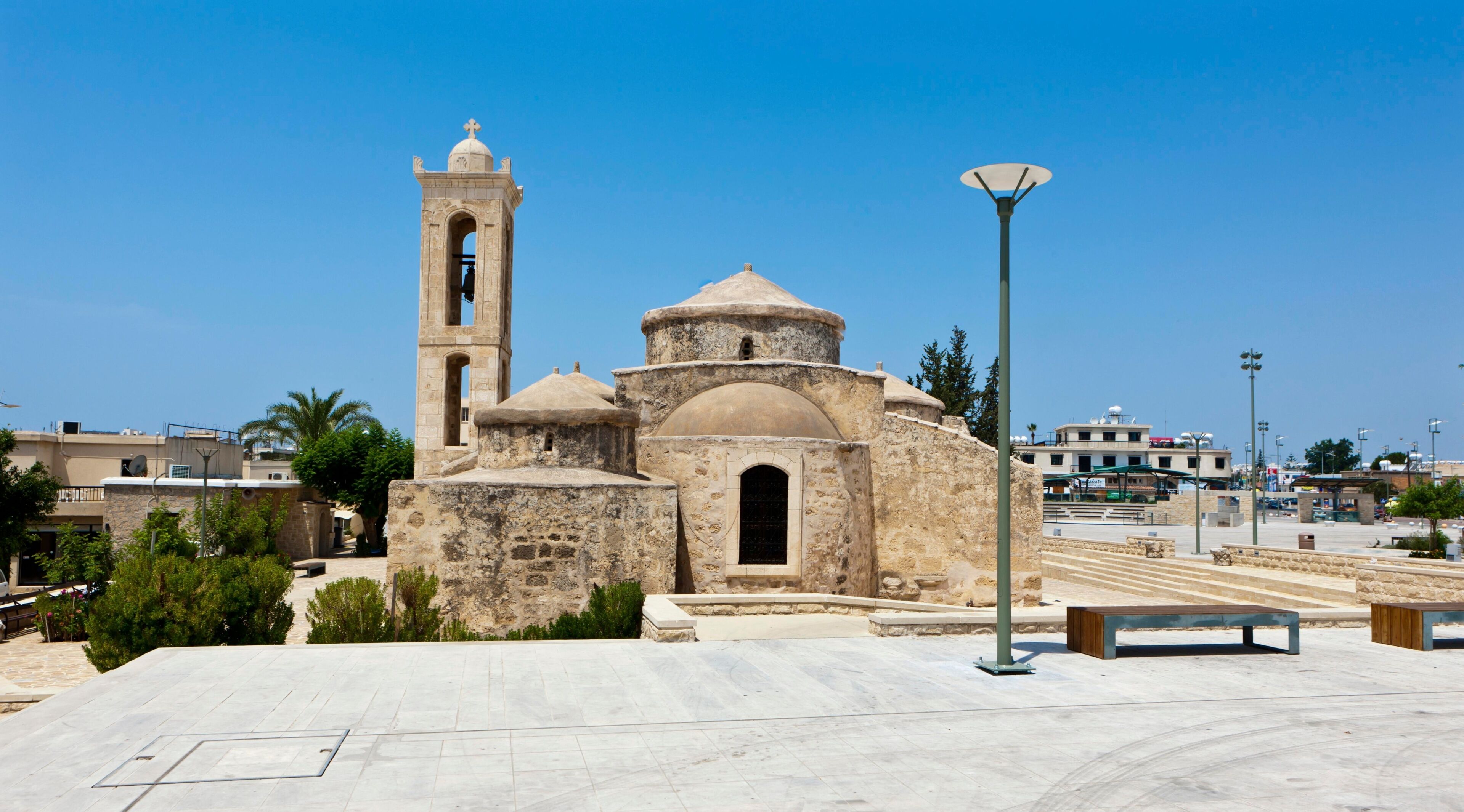 A historic stone church with a bell tower, a dome, and a large open plaza with benches.
