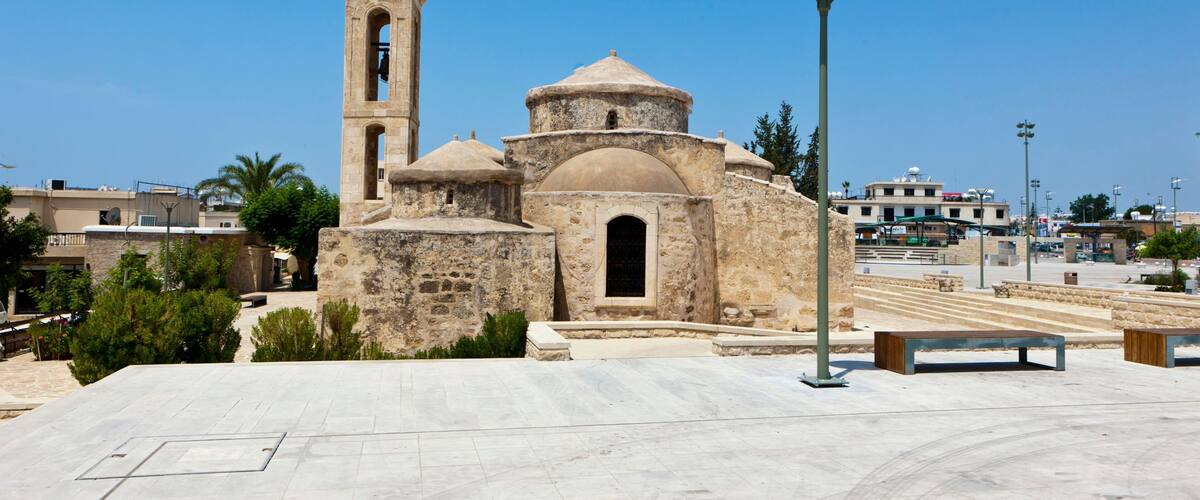 A historic stone church with a bell tower, a dome, and a large open plaza with benches.