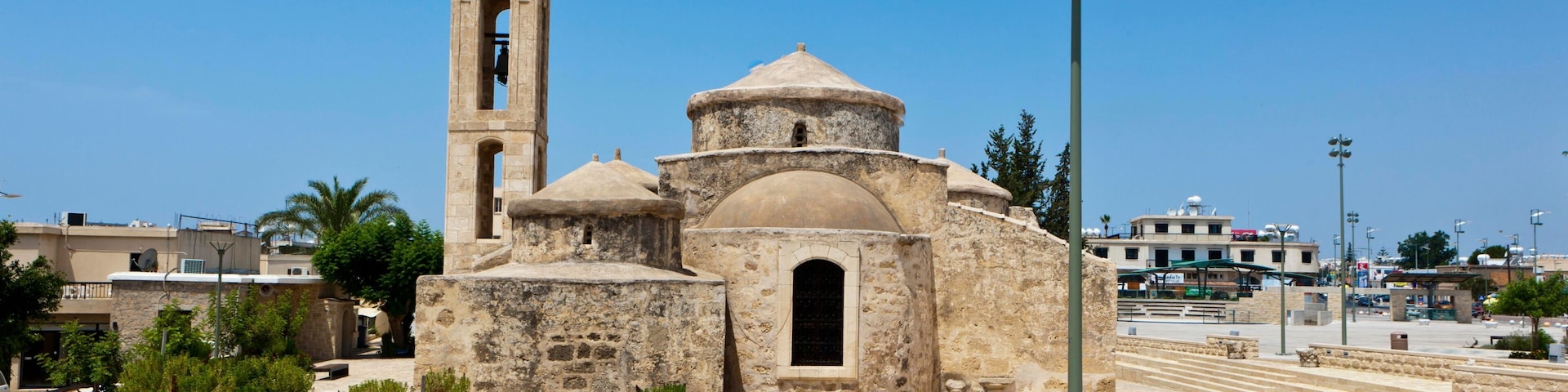 A historic stone church with a bell tower, a dome, and a large open plaza with benches.