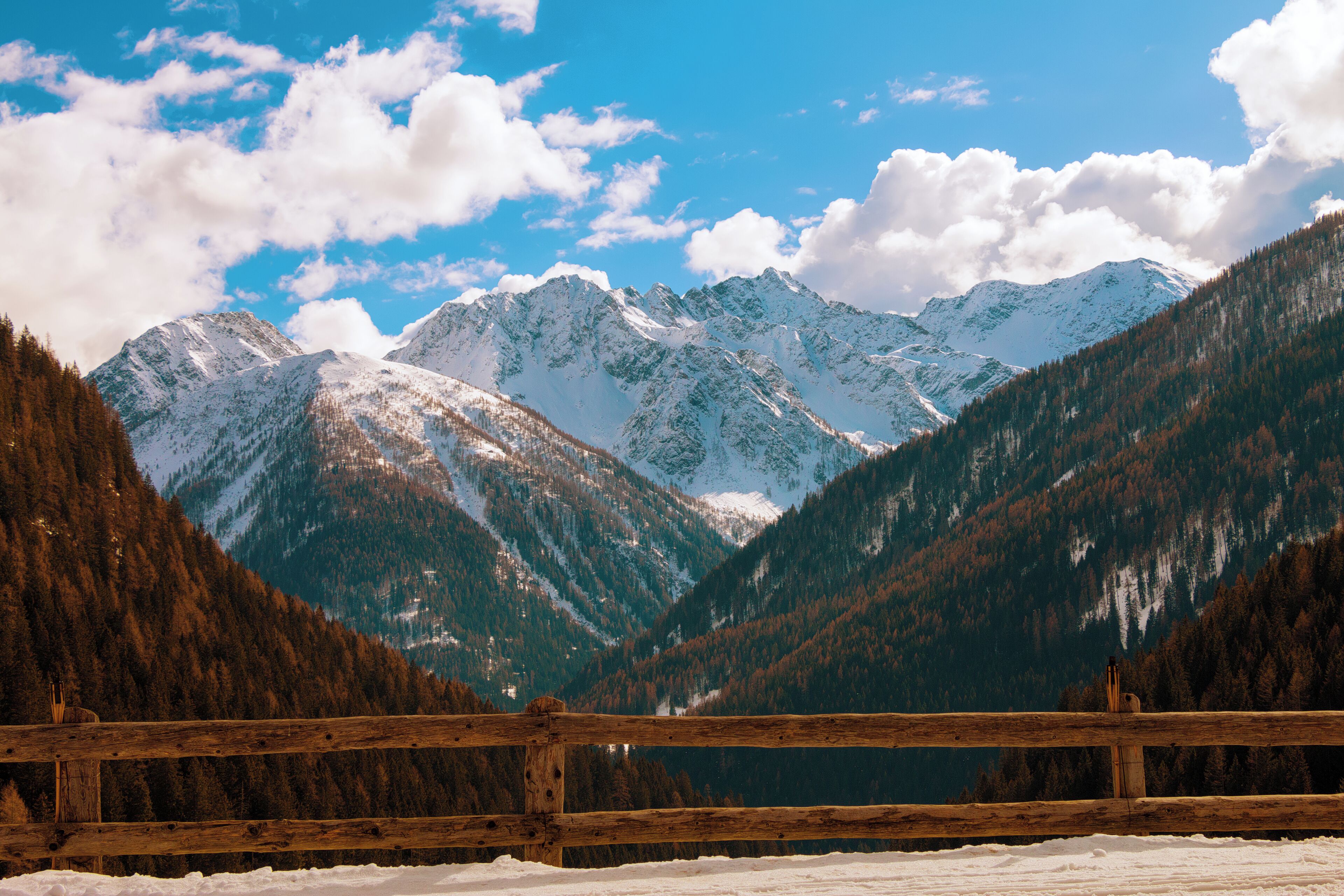 A snow-covered mountain range with a wooden fence in the foreground.