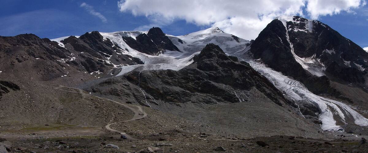 A rugged mountain landscape with a winding dirt road and a snow-capped peak.
