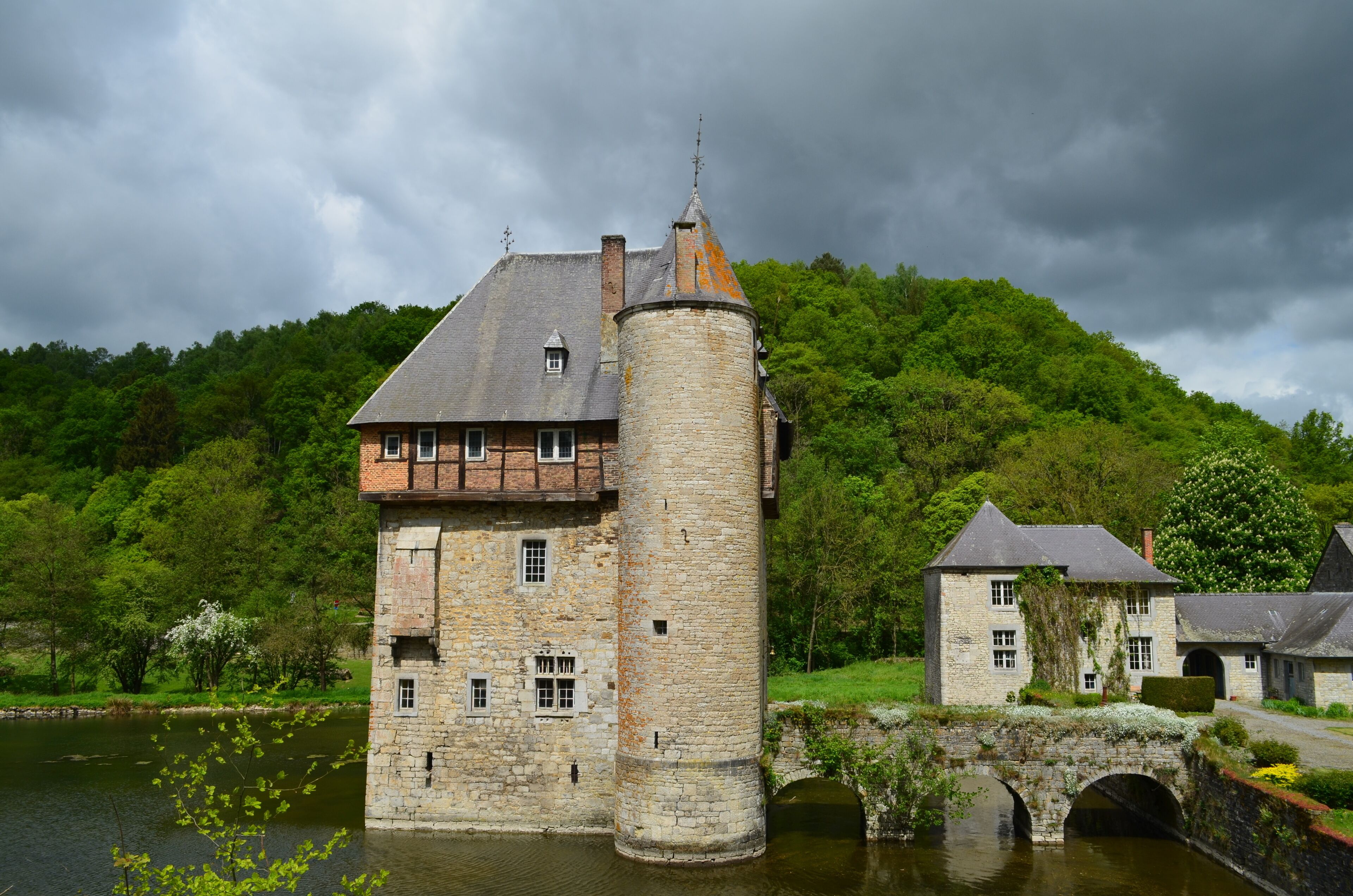 A historic stone castle with a tower, a bridge, and lush green hills in the background.