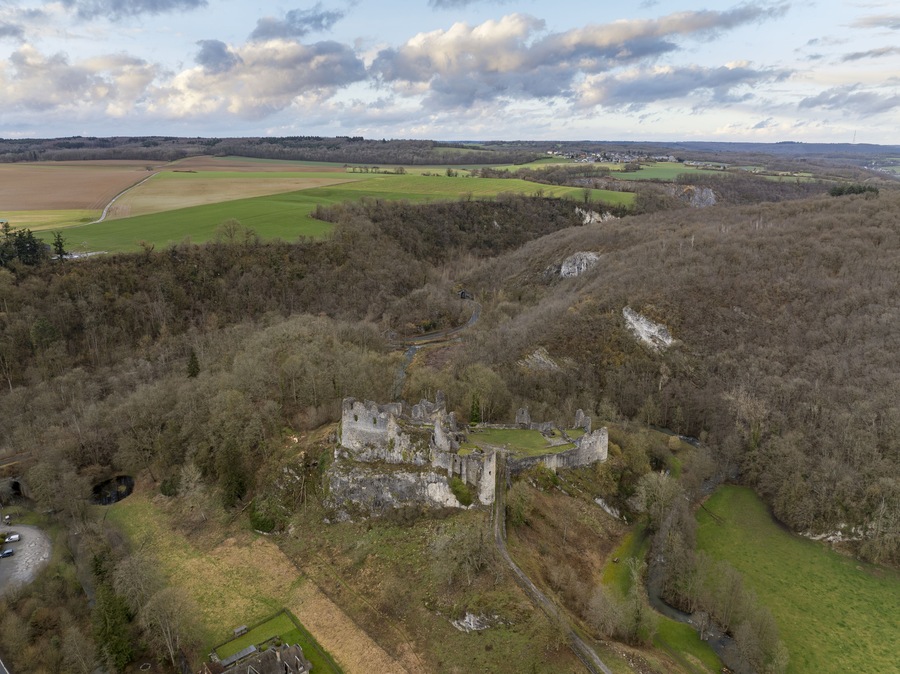 Aerial view of the historic ruins of the Chateau de Crevecoeur perched on a rocky cliff surrounded by dense forest and green fields in Onhaye, Wallonia, Belgium.