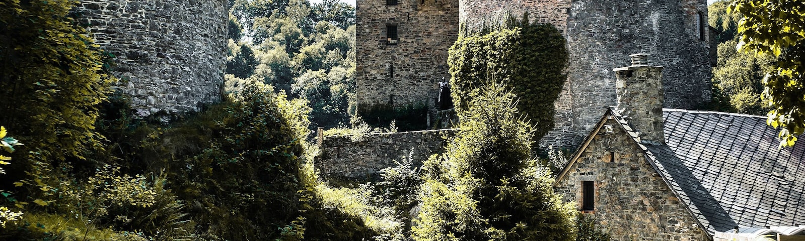 Un castillo de piedra histórico con una torre redonda y un edificio más pequeño con tejado de tejas.