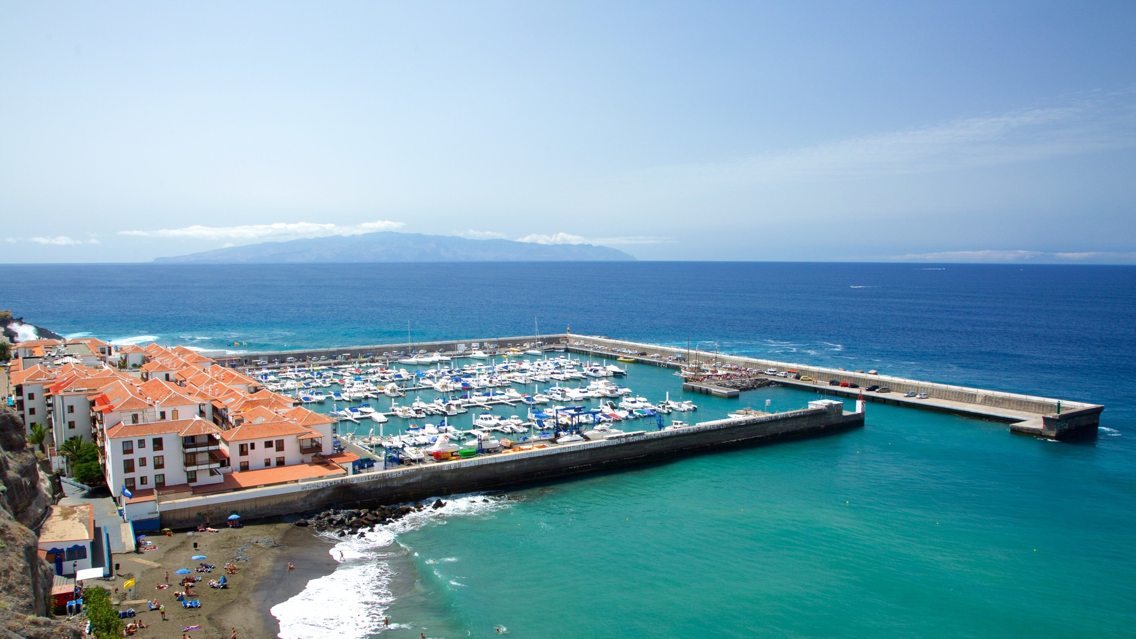 A coastal town with a marina, beach, and buildings with red-tiled roofs.