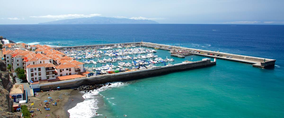 A coastal town with a marina, beach, and buildings with red-tiled roofs.