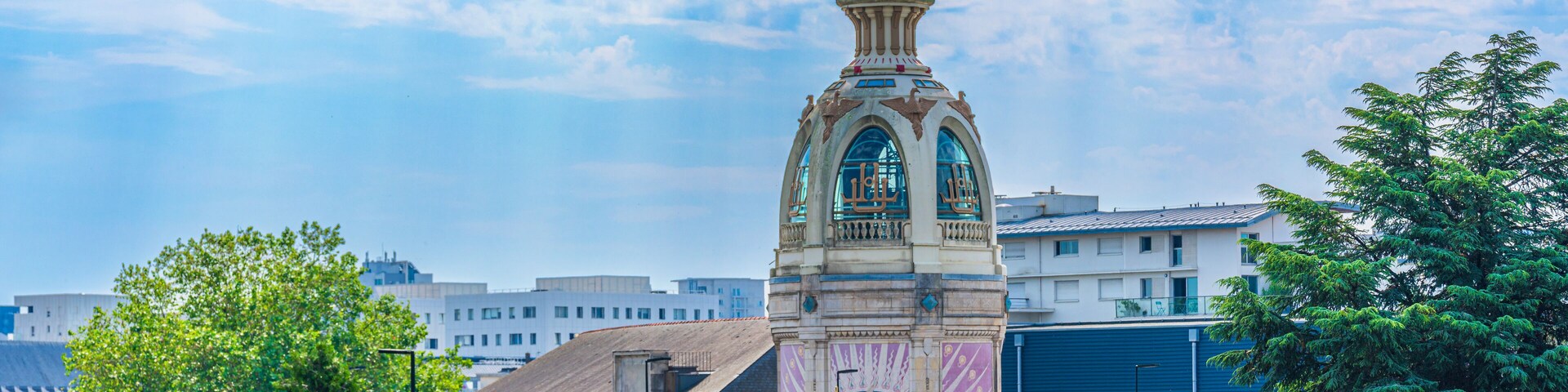Un edificio histórico con una torre del reloj, rodeado de árboles y un puente.