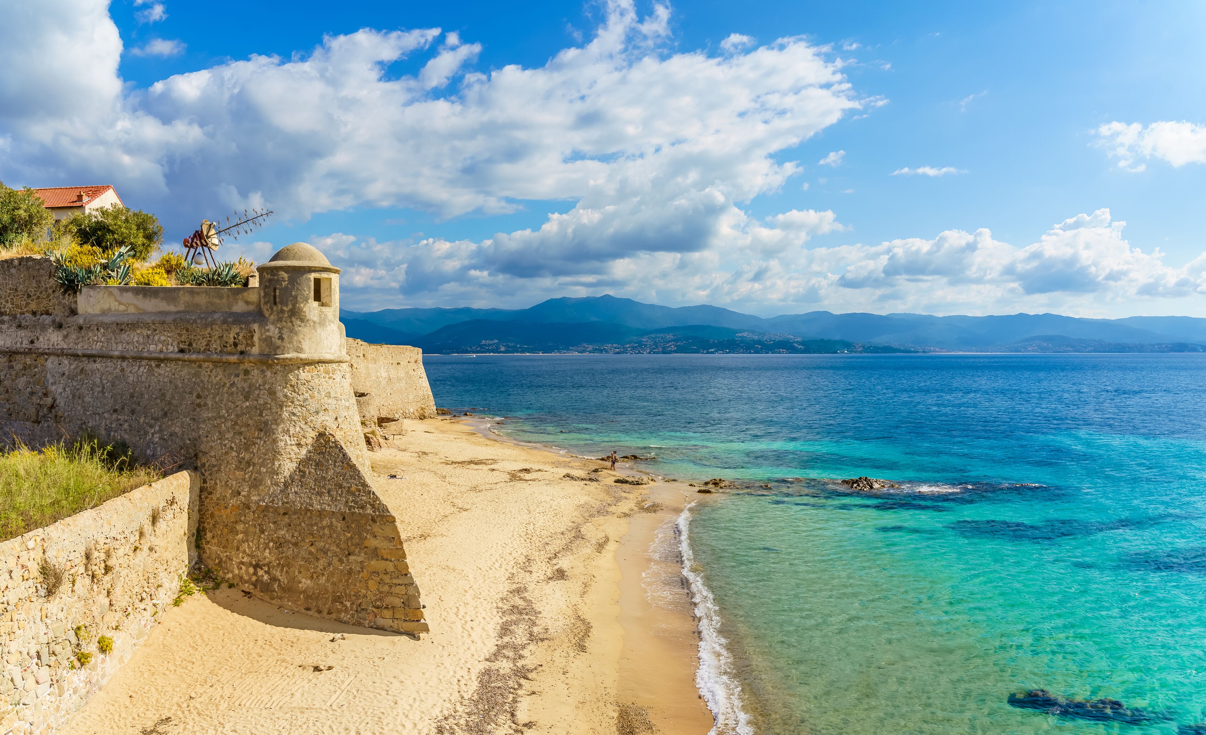 A coastal fortification with a clear view of the sea and distant mountains.