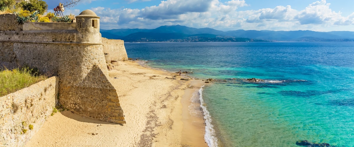 A coastal fortification with a clear view of the sea and distant mountains.