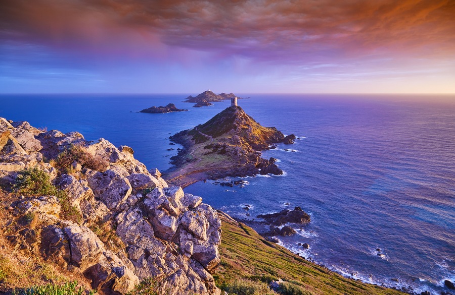 View of Pointe de la Parata on the west coast of Corsica France Europe. A ruined Genoese tower sits on top of the rocky promontory overlooking the archipelago of the Sanguinaires on the colored sunset