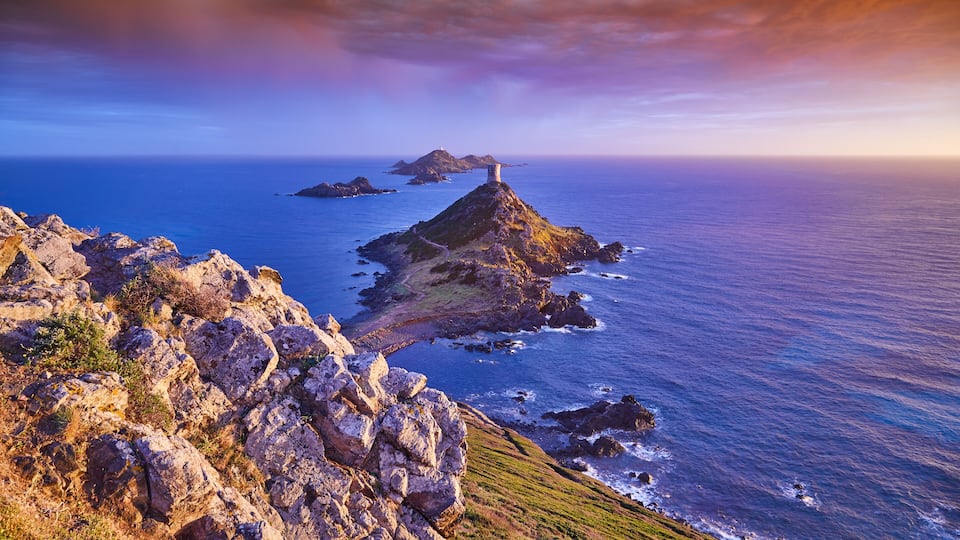 A rugged coastline with rocky outcrops and a lighthouse on a small island.