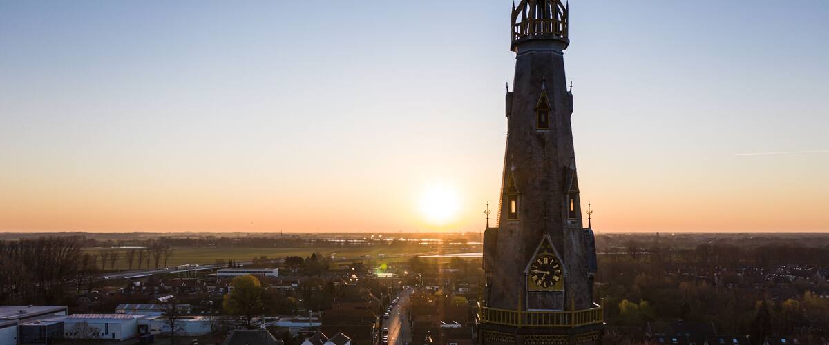 A clock tower with a spire, surrounded by a town with buildings and a road leading to the horizon.