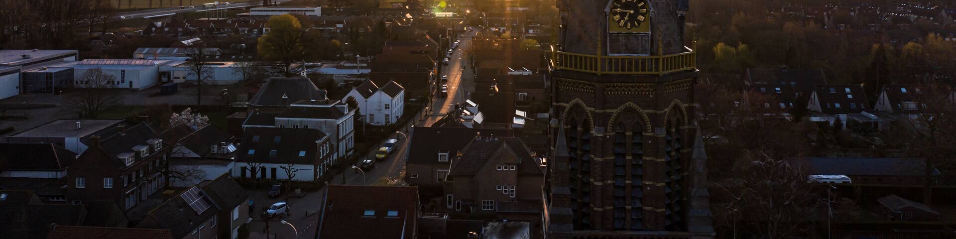 A clock tower with a spire, surrounded by a town with buildings and a road leading to the horizon.