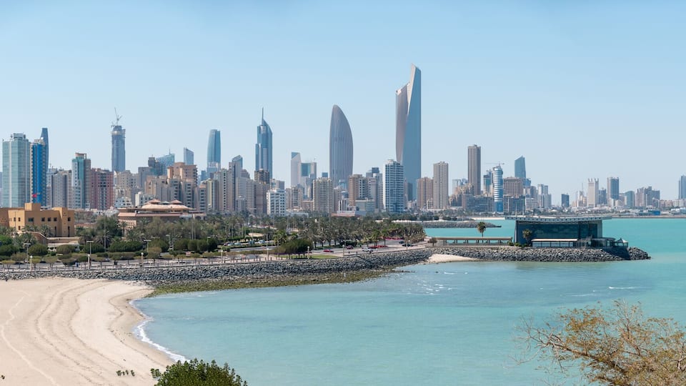 A coastal cityscape with a prominent skyscraper, a sandy beach, and a calm sea.