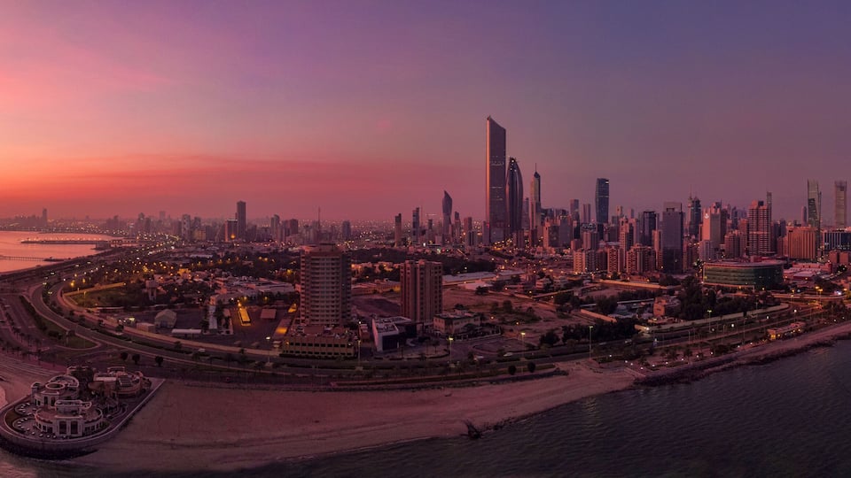 A city skyline at sunset with modern skyscrapers and a waterfront promenade.